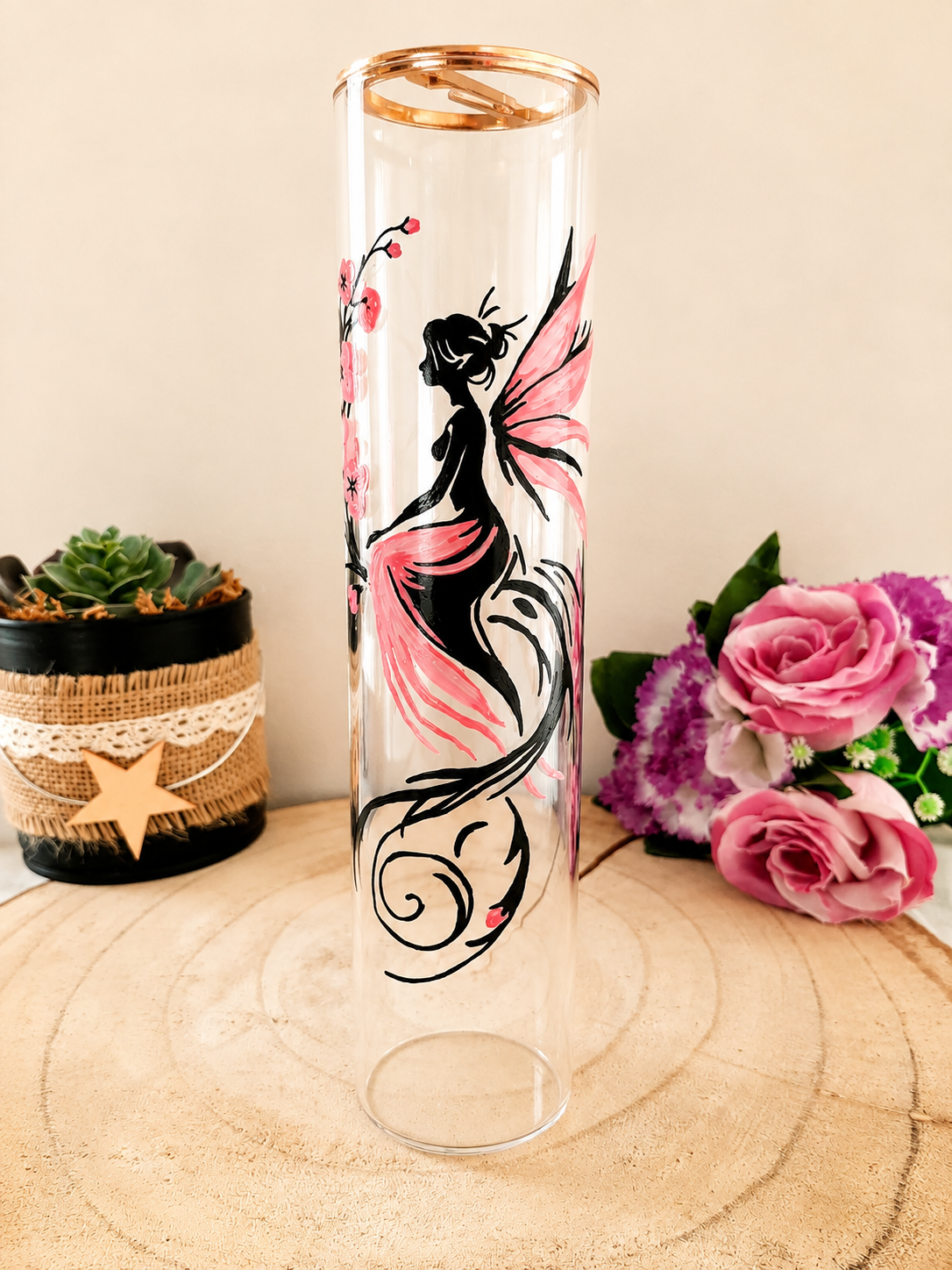 Porte-encens cylindrique en verre peint à la main avec fée aux ailes roses et fleurs de cerisier, cerclage doré, posé sur une table en bois avec des roses roses