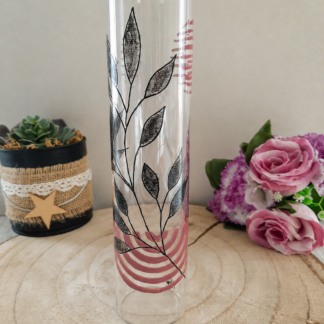 Porte-encens cylindrique en verre peint à la main avec feuillage graphique noir et arcs roses, cerclage argenté, posé sur une table en bois avec des roses roses