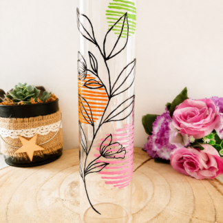 Porte-encens cylindrique en verre peint à la main avec fleurs linéaires noires et touches de couleur vert orange rose, cerclage doré, posé sur une table en bois avec des roses roses