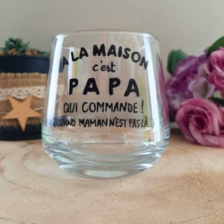Verre à message humoristique peint à la main "À la maison c'est papa qui commande, quand maman n'est pas là", posé sur une table en bois avec des fleurs roses