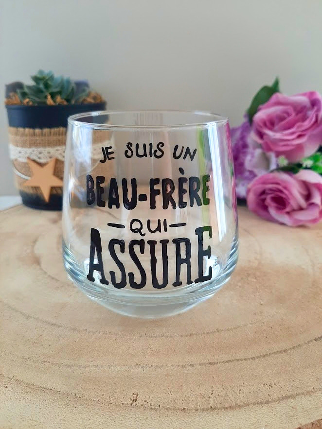 Verre à message peint à la main "Je suis un beau-frère qui assure", posé sur une table en bois avec des fleurs roses