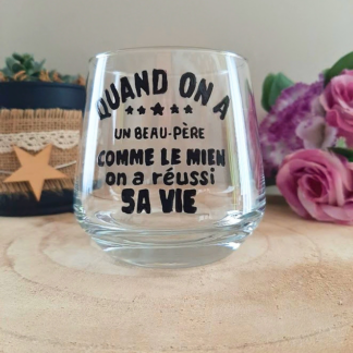 Verre à message peint à la main "Quand on a un beau-père comme le mien on a réussi sa vie" avec petites étoiles, posé sur une table en bois avec des fleurs roses