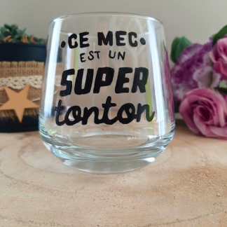 Verre à message peint à la main "Ce mec est un super tonton", posé sur une table en bois avec des fleurs roses