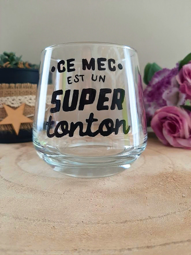 Verre à message peint à la main "Ce mec est un super tonton", posé sur une table en bois avec des fleurs roses