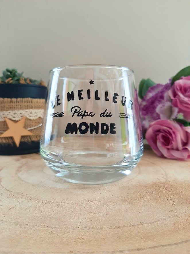 Verre à message peint à la main "Le meilleur papa du monde" style graphique avec vaguelettes, posé sur une table en bois avec des fleurs roses