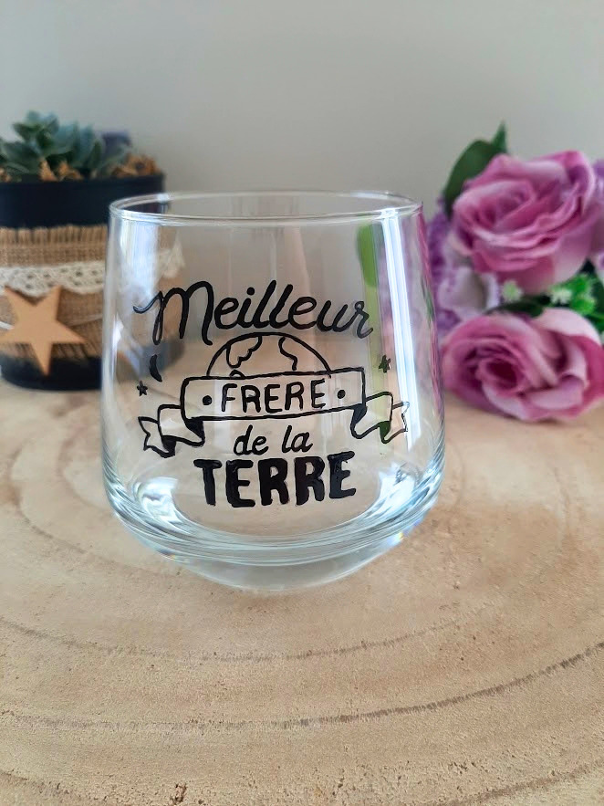 Verre à message peint à la main "Meilleur frère de la Terre" avec illustration de globe terrestre, posé sur une table en bois avec des fleurs roses