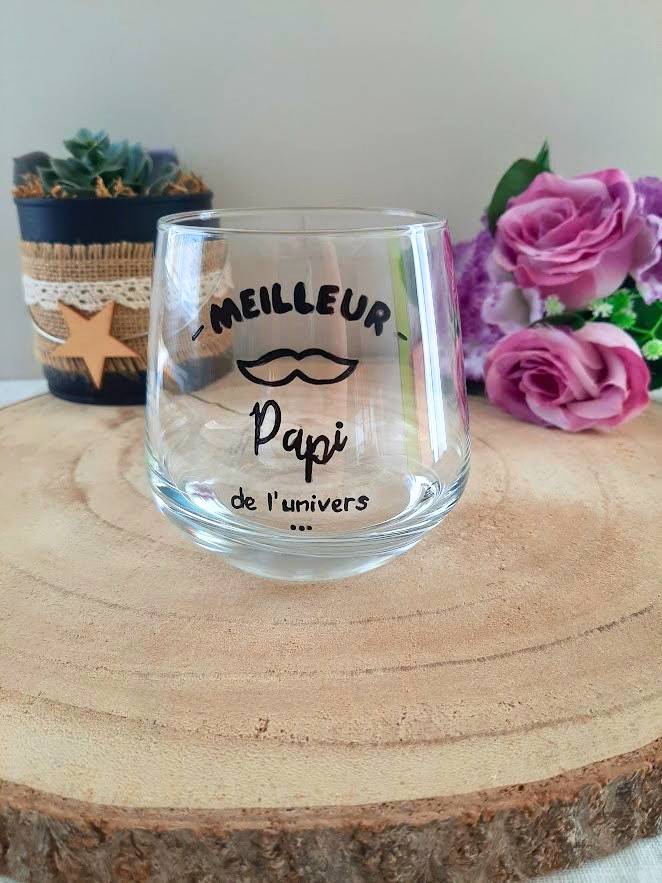 Verre à message peint à la main "Meilleur Papi de l'univers" avec petite moustache illustrée, posé sur une table en bois avec des fleurs roses