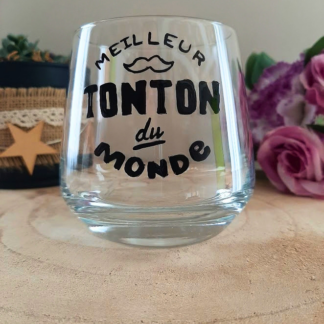 Verre à message peint à la main "Meilleur tonton du monde" avec petite moustache illustrée, posé sur une table en bois avec des fleurs roses