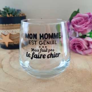 Verre à message humoristique peint à la main "Mon homme est génial mais faut pas le faire chier", posé sur une table en bois avec des fleurs roses