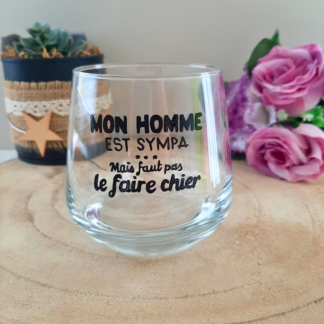 Verre à message humoristique peint à la main "Mon homme est sympa mais faut pas le faire chier", posé sur une table en bois avec des fleurs roses