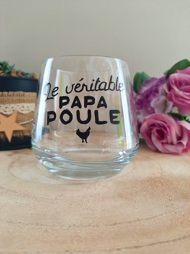 Verre à message peint à la main "Le véritable papa poule" avec petite poule illustrée, posé sur une table en bois avec des fleurs roses