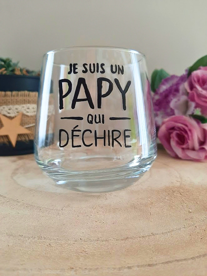 Verre à message peint à la main "Je suis un papy qui déchire", posé sur une table en bois avec des fleurs roses