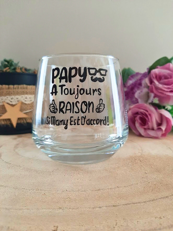 Verre à message humoristique peint à la main "Papy a toujours raison si Mamy est d'accord" avec illustrations lunettes et pouces levés, posé sur une table en bois avec des fleurs roses