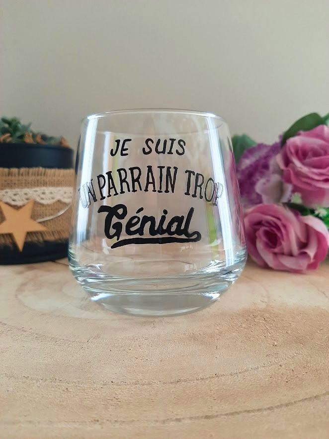 Verre à message peint à la main "Je suis un parrain trop génial", posé sur une table en bois avec des fleurs roses