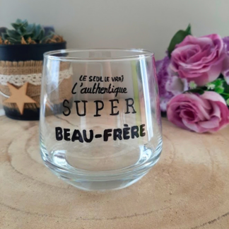 Verre à message peint à la main "Le seul, le vrai, l'authentique super beau-frère", posé sur une table en bois avec des fleurs roses