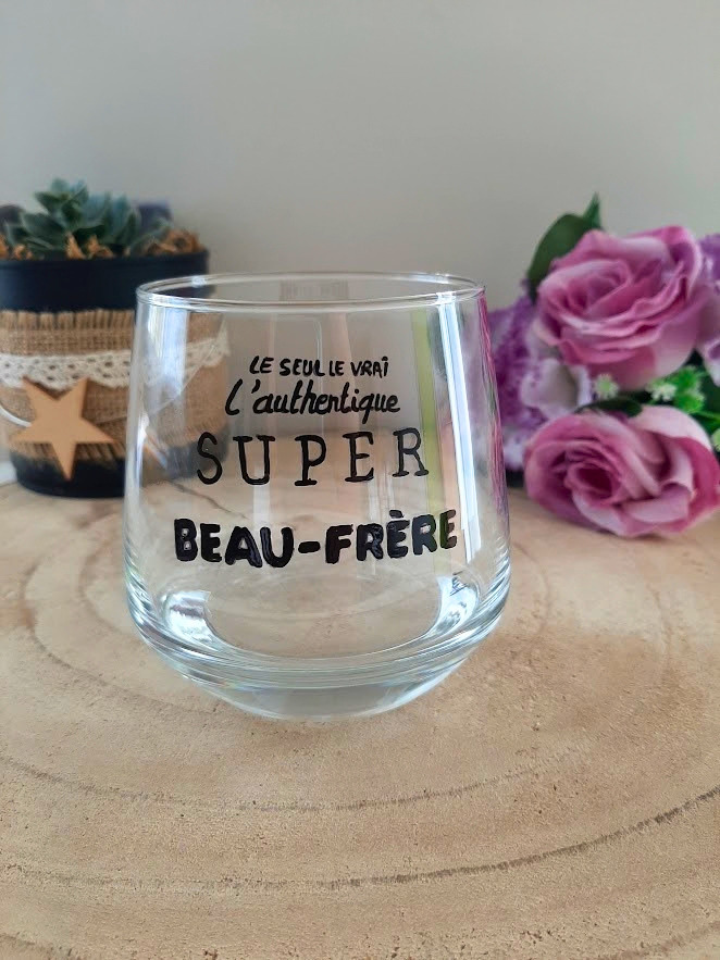 Verre à message peint à la main "Le seul, le vrai, l'authentique super beau-frère", posé sur une table en bois avec des fleurs roses