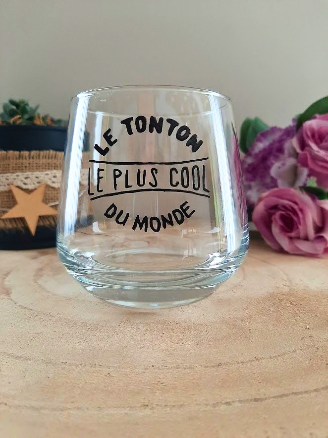 Verre à message peint à la main "Le tonton le plus cool du monde", posé sur une table en bois avec des fleurs roses